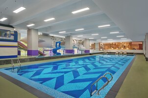 Una piscina interior con un diseño geométrico de azulejos, una zona de juegos infantiles y un bar con asientos.
