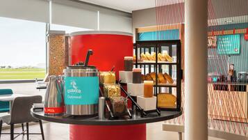 A breakfast bar with Quaker Oatmeal and milk, a coffee machine, and a display of pastries.
