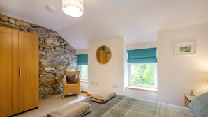 Une chambre avec un mur en pierre, une armoire en bois, un lit recouvert d’une courtepointe à rayures, une chaise et une fenêtre donnant sur un paysage agréable.