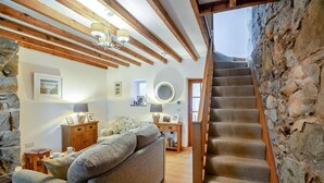 Un salon avec un canapé, des poutres en bois, des murs en pierre, un escalier et une vue sur le ciel.