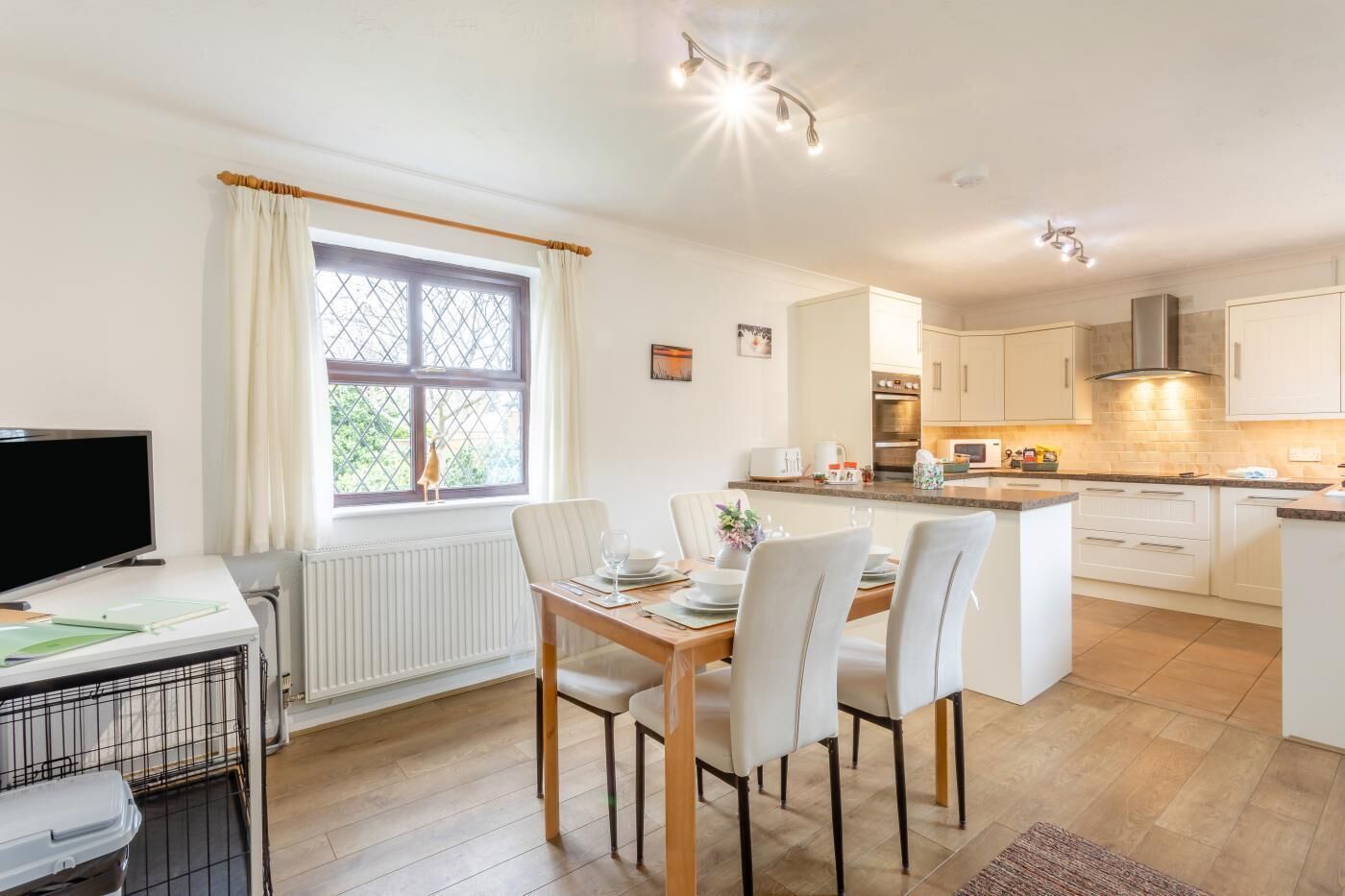 A modern kitchen with white cabinets, a dining area with a table and chairs, and a large window with curtains.