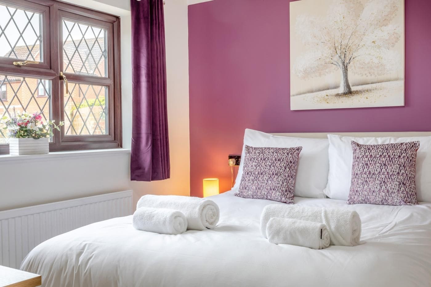 A bedroom with a bed, pillows, a window with curtains, and a wall painting.
