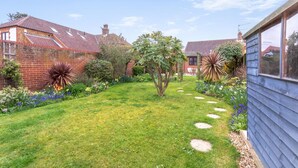 Ein gepflegter Garten mit einem Pflasterweg, verschiedenen Pflanzen und einem Backsteinhaus mit Ziegeldach.