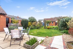 Eine Terrasse mit Tisch und Stühlen, ein grüner Garten und ein Backsteinhaus.