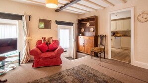 A living room with a red sofa, a wooden cabinet, a dining area with a table and chairs, and a kitchen visible through an open door. - 1 Bed in Castleton (oc-s36309) (Castleton)