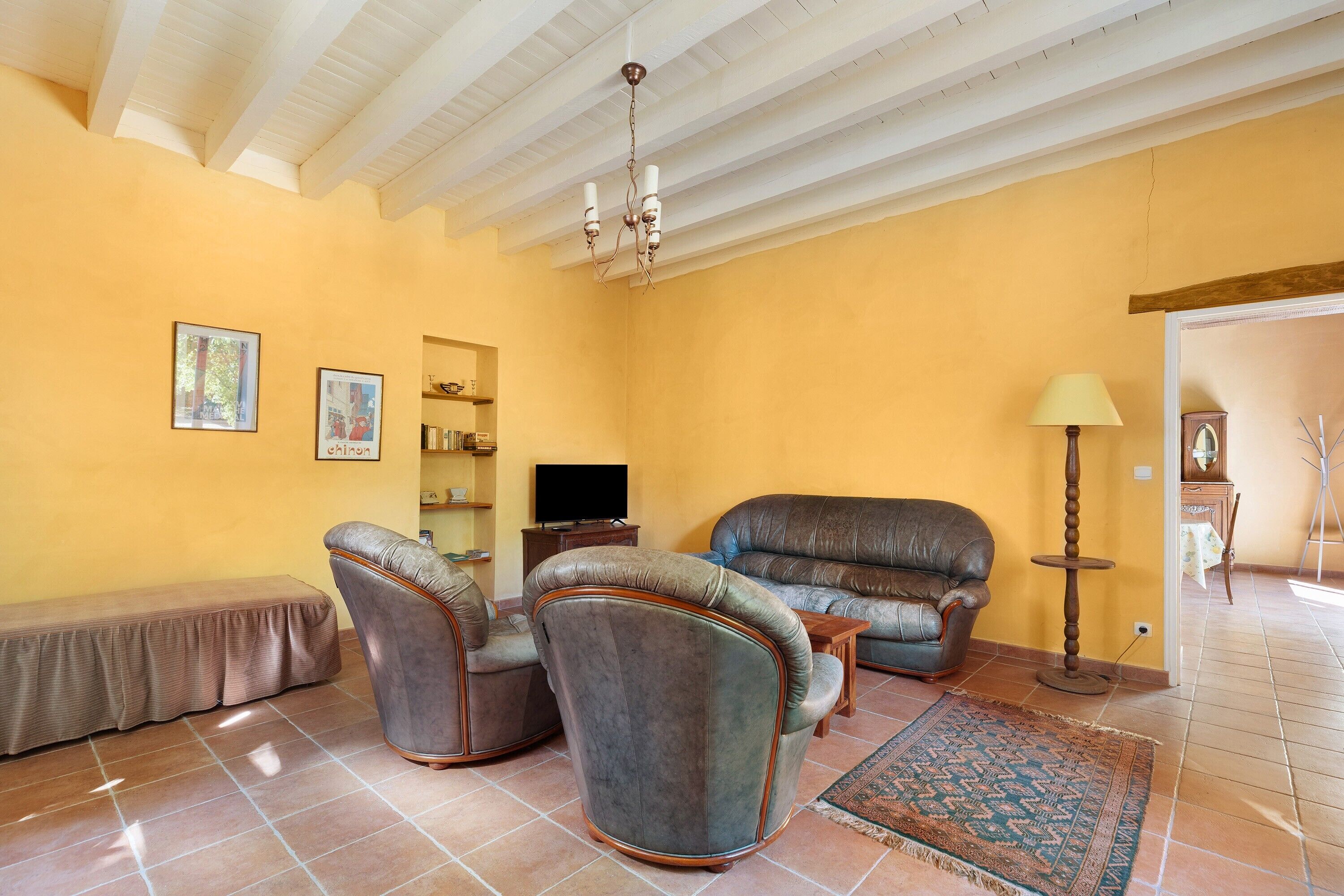 A living room with a sofa, two armchairs, a bench, a television, and a lamp.