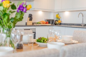 Eine moderne Küche mit Essbereich, inklusive Kücheninsel, Esstisch gedeckt mit Tellern, Gläsern und einer Blumenvase.