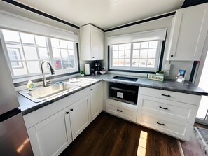 Una cocina moderna con armarios blancos, un lavamanos de acero inoxidable, un horno empotrado y una cafetera.