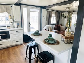 Una cocina moderna con una isla central, un área de comedor con un sofá y vistas por una puerta abierta.