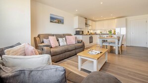 Ein modernes Wohnzimmer mit Sofa, Couchtisch und einem Essbereich, wobei im Hintergrund eine Küche zu sehen ist.