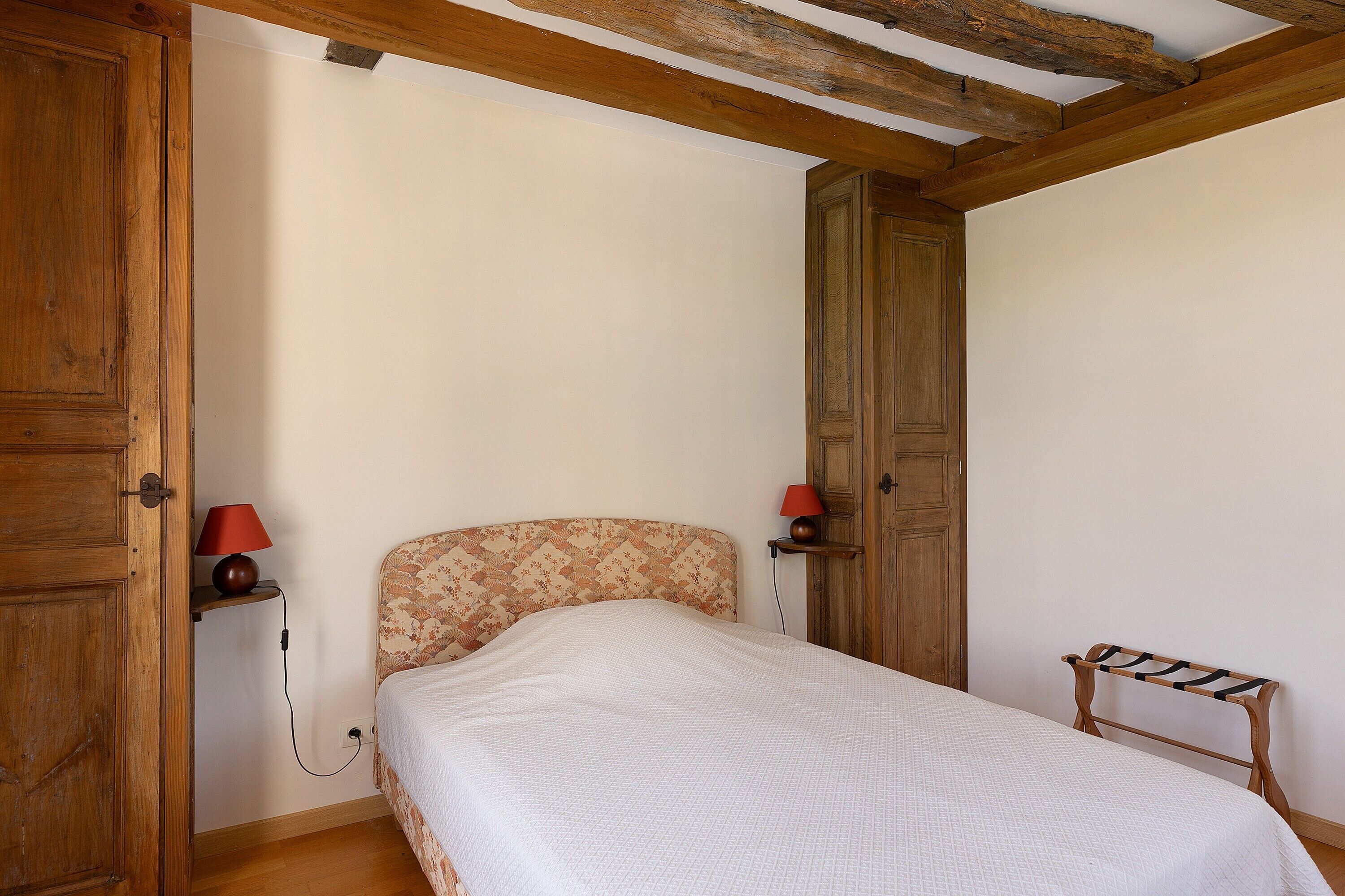 Een slaapkamer met een bed, houten hoofdbord, twee bedlampen, een houten garderobe en een houten plank met een lamp.