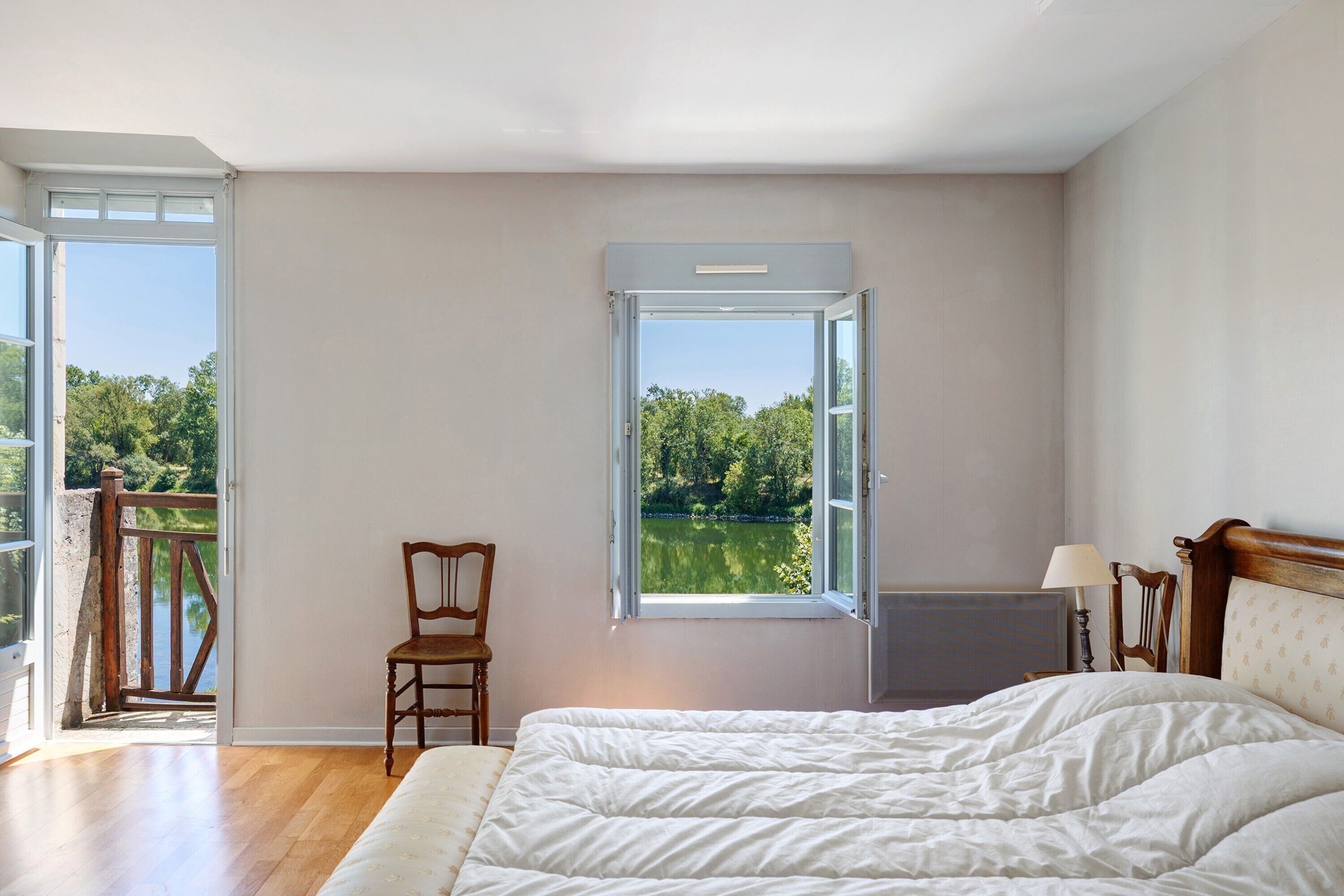 Una camera da letto con un letto, una sedia, una finestra vista lago e un balcone.
