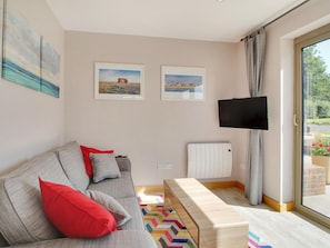 Ein modernes Wohnzimmer mit einer Couch, einer Bank, einem Flachbildfernseher und zwei gerahmten Bildern an der Wand.