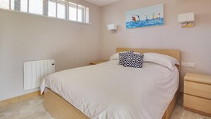 A bedroom with a bed, a nightstand, a wall-mounted light, a painting of sailboats, and a window with blinds. - 1 Bed in Tenterden (oc-79130) (Tenterden)