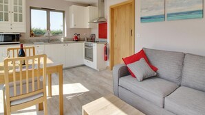 A modern kitchen with white cabinets, a red kettle, and a dining area with a wooden table and chairs. - 1 Bed in Tenterden (oc-79130) (Tenterden)