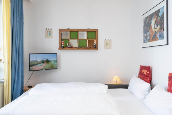 A hotel room with a bed, a television, a shelf with decorative items, and a painting on the wall. - Ostseeurlaub zu Zweit - Ferienwohnung in Sellin mit Balkon (Sellin)