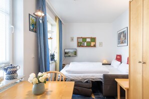 Ein Zimmer mit einem Bett, einem Tisch mit Blumenvase, einem Sessel, einem Holzschrank und einem Fenster mit Vorhängen.