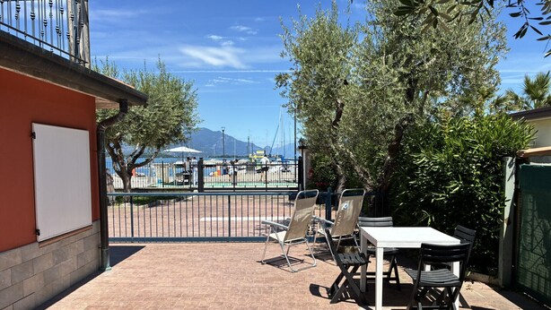 An outdoor patio with a table and chairs, a view of the sea, and a mountain in the background. - Spiaggia Apartment by Booking Lake Garda (Manerba del Garda)
