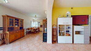 A spacious living area with a dining table, kitchen, and a TV on a stand. - Spiaggia Apartment by Booking Lake Garda (Manerba del Garda)