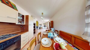 A kitchen with a gas stove, wooden cabinets, and a dining area with a table set for two. - Spiaggia Apartment by Booking Lake Garda (Manerba del Garda)