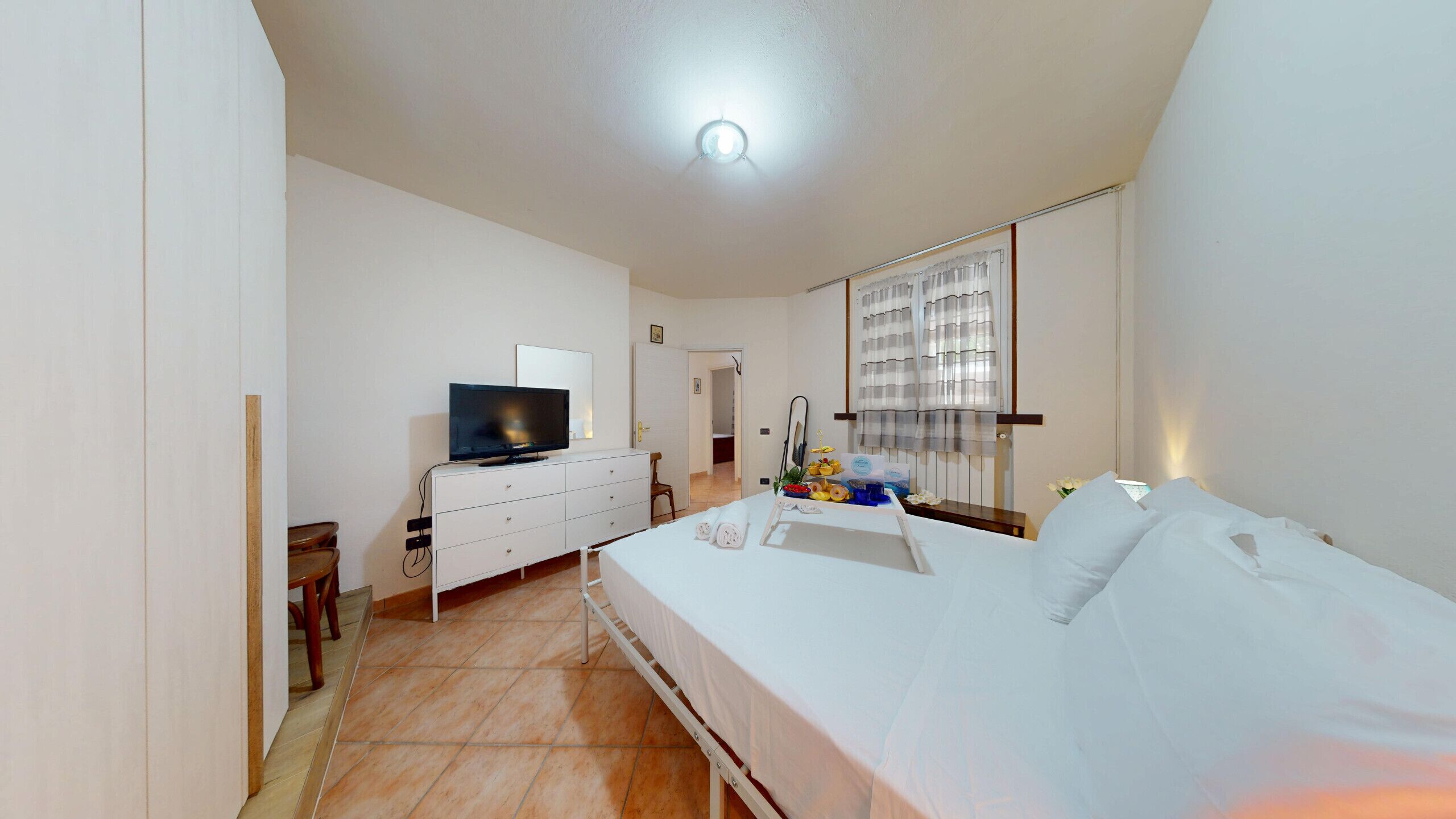 Quarto de hotel com uma cama, televisão, penteadeira e banheiro visível por uma porta aberta.