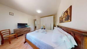 A bedroom with a bed, wooden furniture, a television, and a painting on the wall. - Spiaggia Apartment by Booking Lake Garda (Manerba del Garda)
