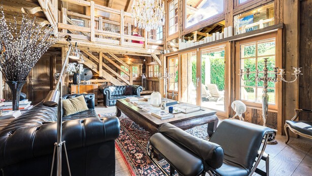 A spacious room with a large wooden ceiling, a black leather sofa, a dining table, and a chandelier. - Chalet Zibeline (Megève)