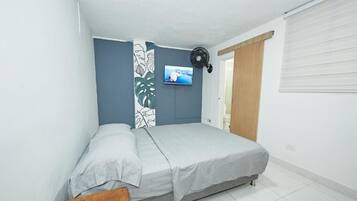 Un dormitorio con cama, televisor montado en la pared y ventana con persianas.