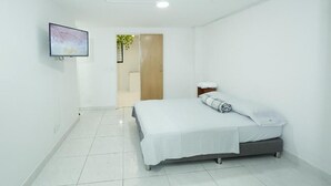 Un dormitorio limpio y moderno con cama, televisor en la pared y puerta que da a otra habitación.