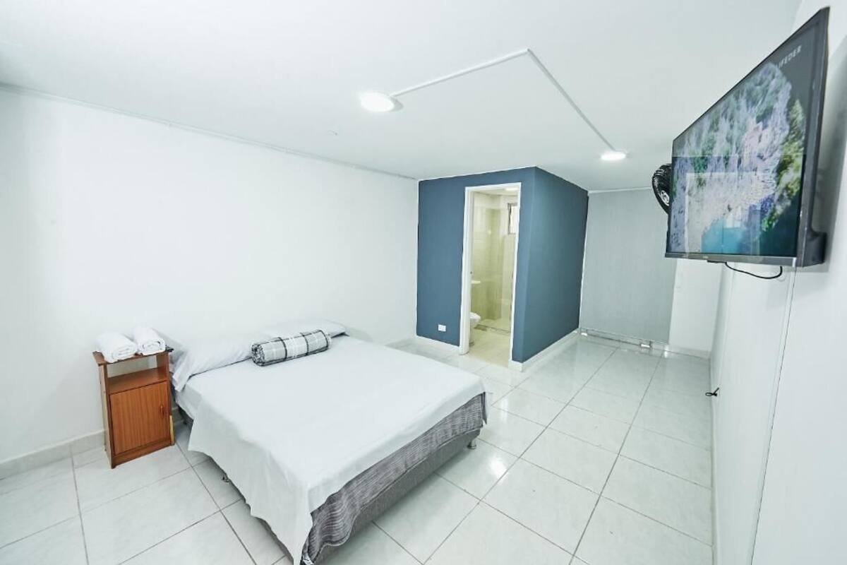 A bedroom with a bed, a wooden nightstand, a TV, and a door leading to a bathroom.