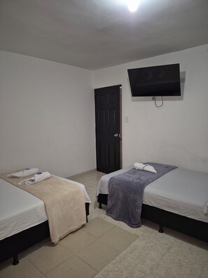 A room with two beds, a TV mounted on the wall, a door, and a tiled floor. - Hostel Casa Host 72 (Medellín)