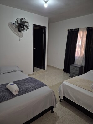 A hotel room with two beds, a standing fan, a dresser, and a door leading to another room. - Hostel Casa Host 72 (Medellín)