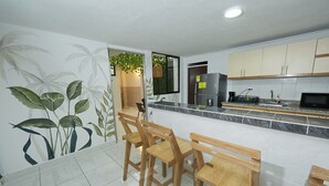 Una cocina con sillas de madera, un refrigerador, un microondas y una ventana con una planta.