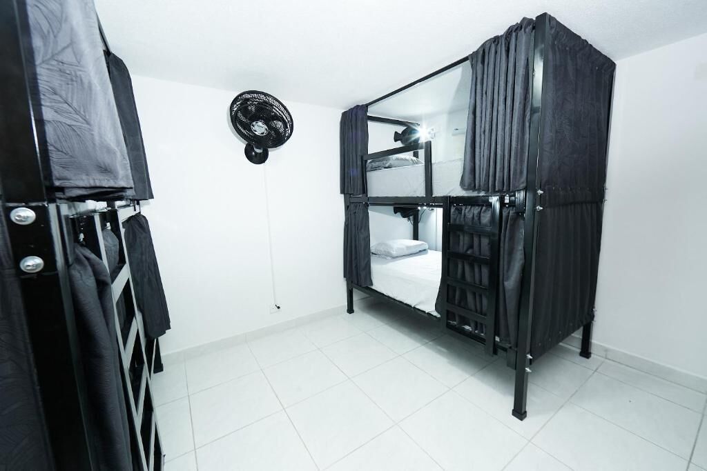 Habitación pequeña con literas, ventilador de techo y armario con ropa colgada.