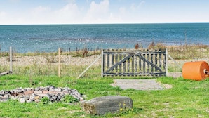 Une vue sur la côte, avec un portail en bois, un sentier pavé de pierres et une zone herbeuse menant à la mer.