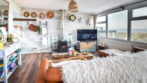 Un salon chaleureux avec une cheminée, un téléviseur et une grande fenêtre donnant sur la mer.