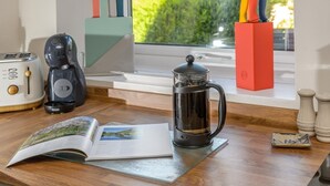 Uma cozinha equipada com cafeteira, prensa francesa, torradeira e uma janela com vista para o verde.