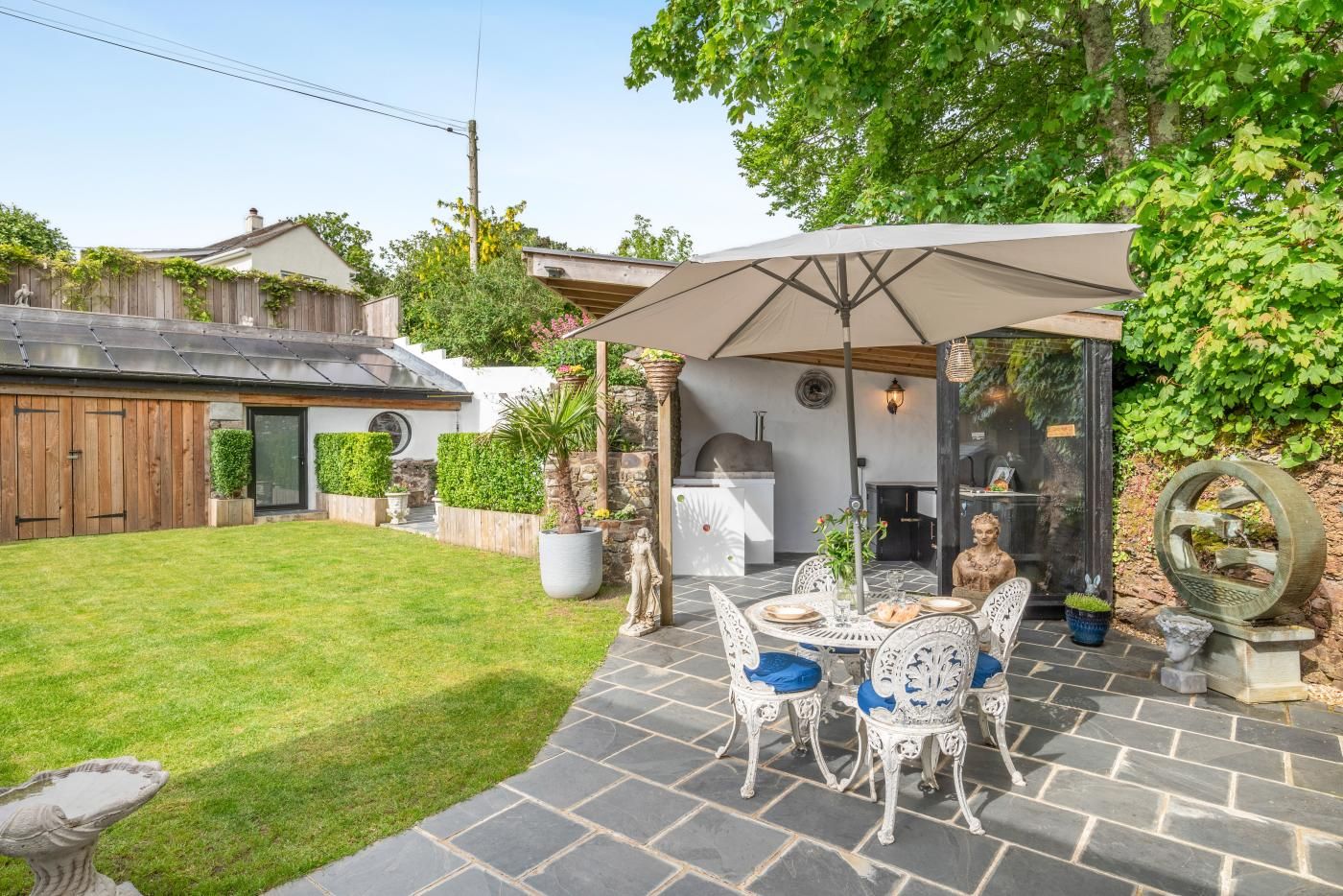 En terrasse med et bord og stole, grillområde og en have.