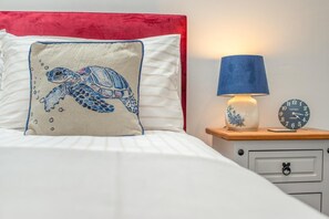 A bed with a red headboard, a pillow with a sea turtle design, a bedside lamp, and a clock on a wooden nightstand. - 1 Bed in Stratton (oc-f35146) (Stratton)