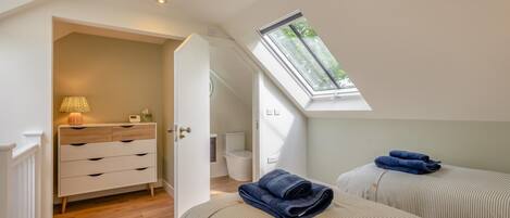 Ein Schlafzimmer mit zwei Betten, einem Nachttisch, einer Lampe, einem Fenster und einer Tür zu einem Badezimmer.