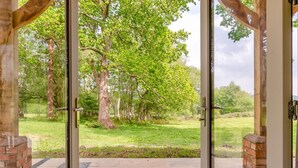 Eine Glastür führt zu einer Terrasse mit Blick auf eine Rasenfläche und Bäume.