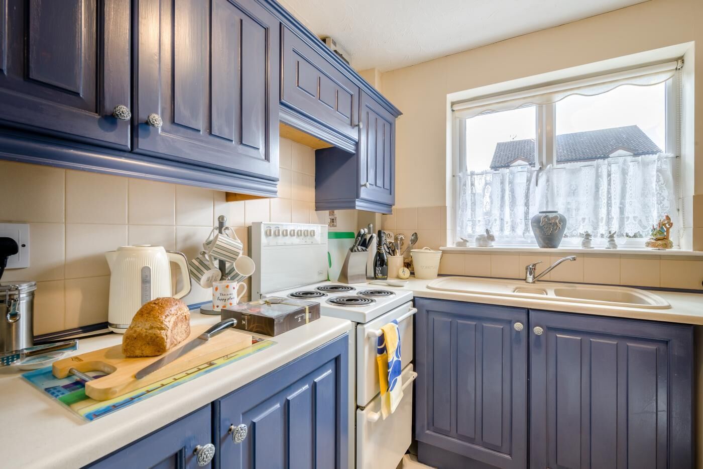 A kitchen with dark blue cabinets, a white stove, and a window with a view of a house.
