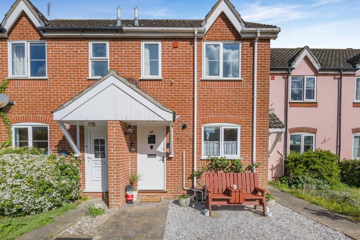 A two-story brick house with a front porch, a small garden, and a wooden bench.
