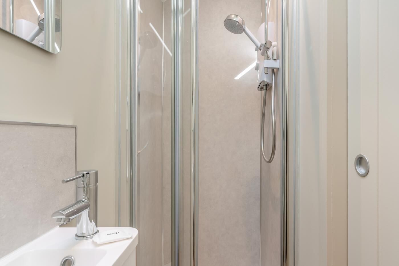 A modern bathroom with a glass-enclosed shower, a white sink with a chrome faucet, and a mirror above the sink.