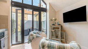 Ein gemütliches Zimmer mit einer großen Schiebeglastür, die auf eine Terrasse im Freien führt, einem an der Wand montierten Flachbildfernseher und einem kleinen Tisch mit dekorativen Accessoires.