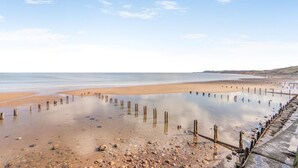 Ein Strand mit Holzpfählen im Wasser, einem sandigen Ufer und einem klaren Himmel.