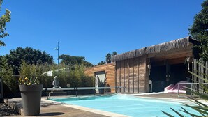 Une terrasse en bois avec une piscine, une structure à toit de chaume et une statue.