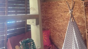 Un intérieur en bois avec un lit superposé, une fenêtre avec des stores, une plante en pot et une tente amérindienne.