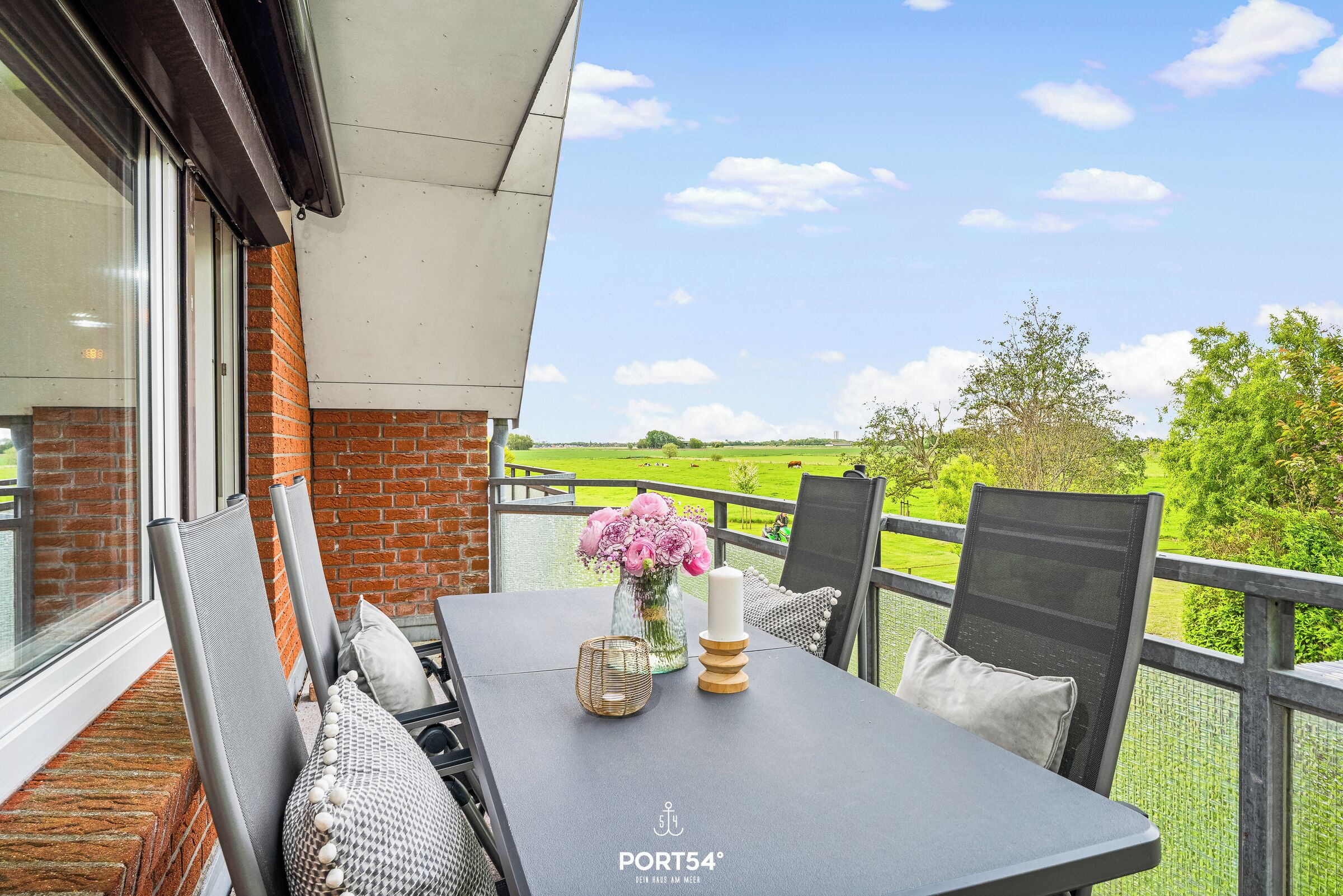 Ein Balkon mit Tisch, Stühlen und Blick auf ein grünes Feld.