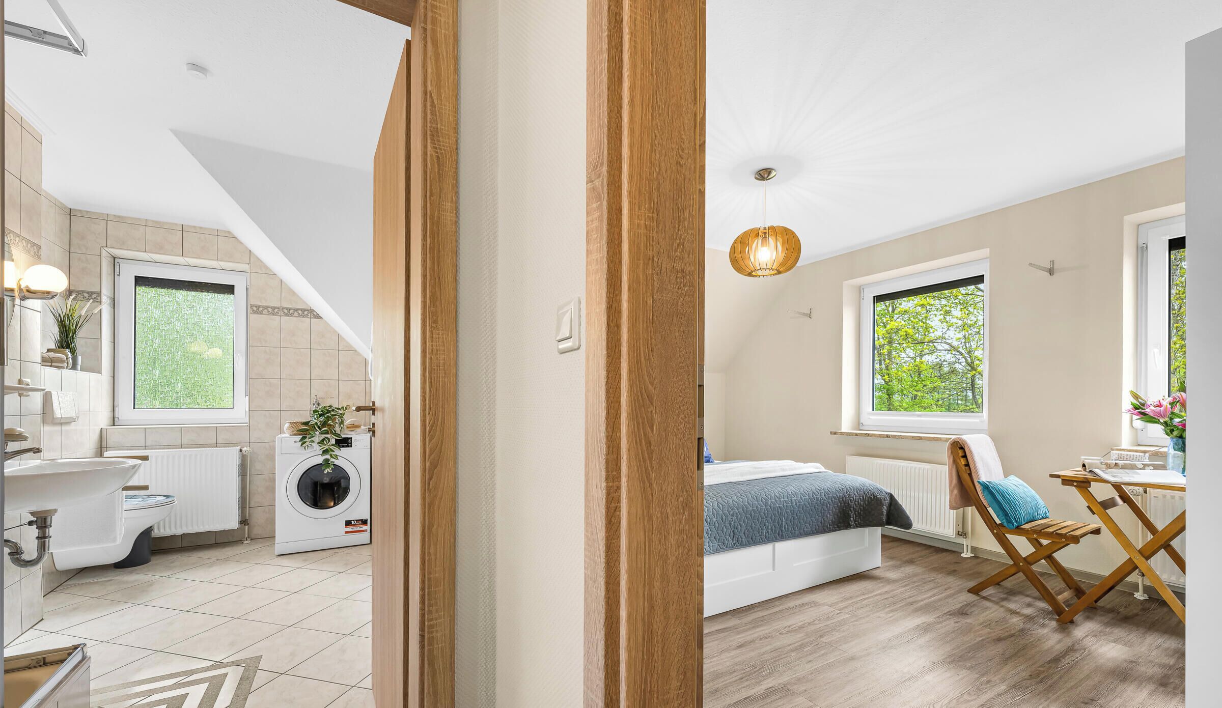 Ein modernes Schlafzimmer mit Bett, Schreibtisch und Stuhl. Ein Fenster bietet Blick auf Bäume.